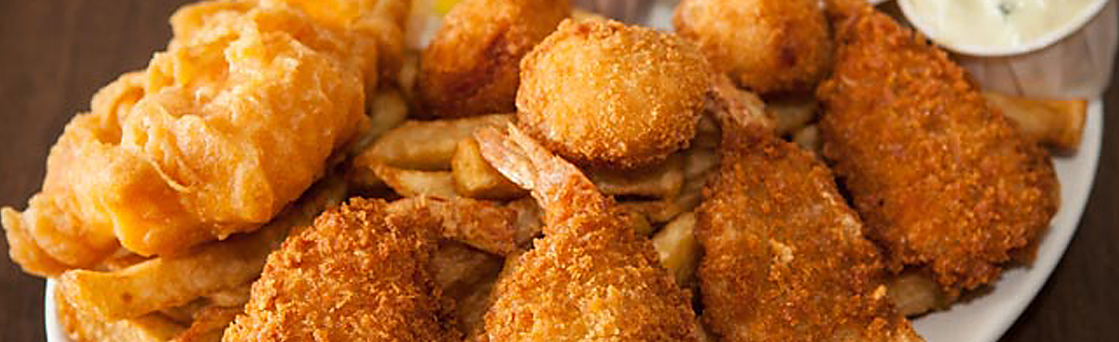 A matte gouache painting-style overhead illustration of a mixed fried seafood platter with golden fries and a small dish of red dipping sauce, in warm golden and brown tones, appetizing and inviting.