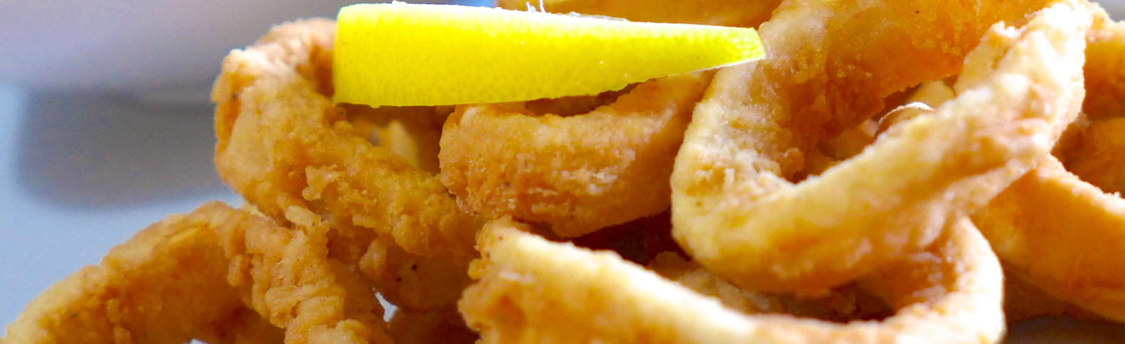Close-up gouache painting of fried calamari rings with a lemon wedge garnish, golden and yellow tones, appetizing mood.