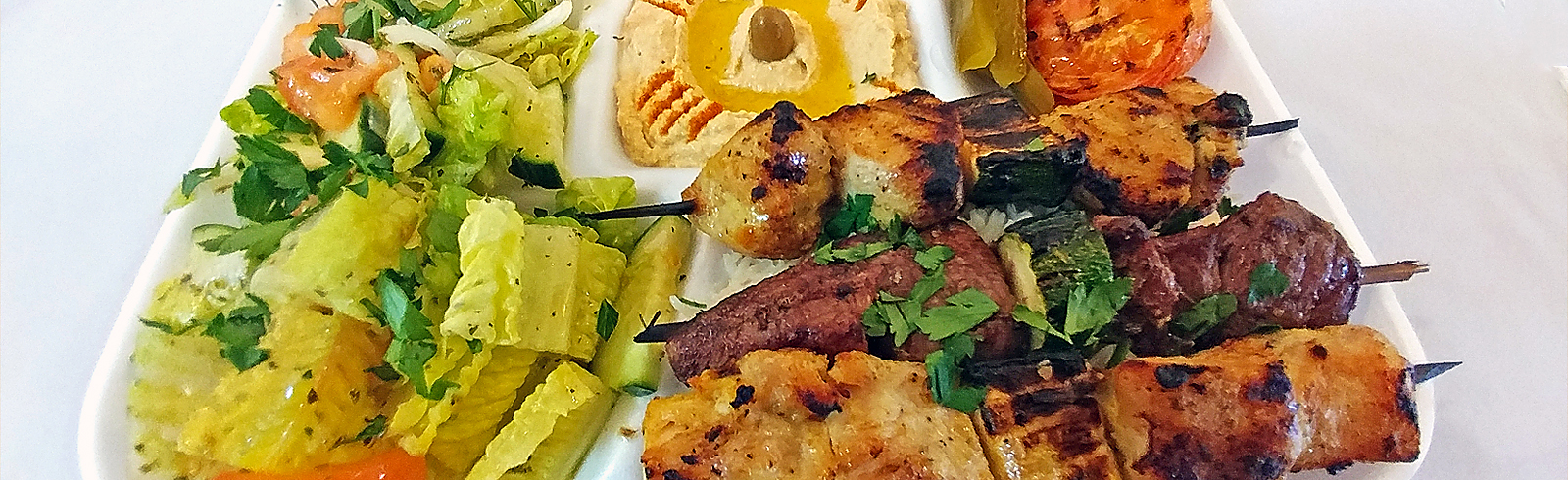 Gouache painting of a platter of grilled meat skewers with salad, hummus and pickles, warm coral and cream tones.
